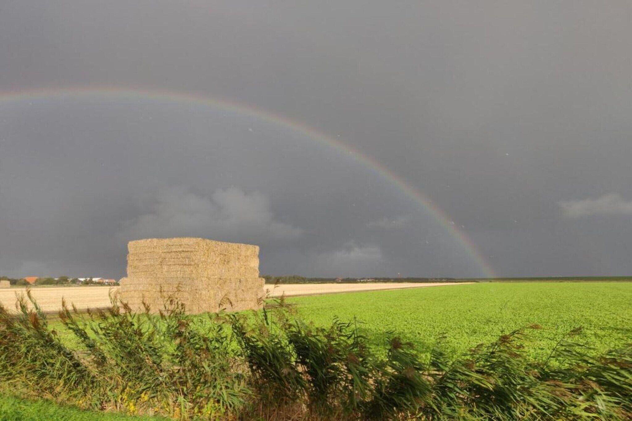 A rural landscape with a haystack and a rainbow.