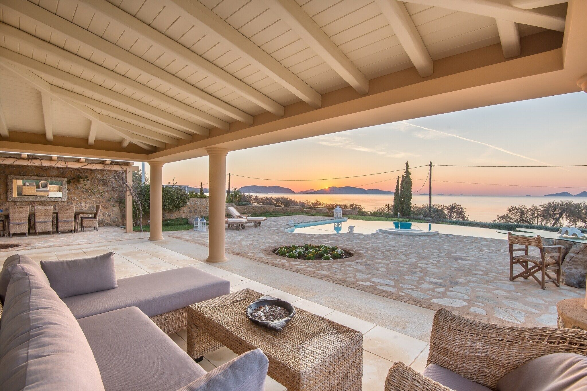 A covered outdoor seating area with a view of the sunset over the water.