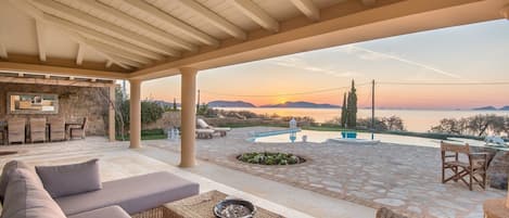 A covered outdoor seating area with a view of the sunset over the water.