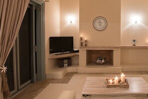 A modern living room with a flat-screen TV, a fireplace, and a clock on the wall. - Villa in Peloponnese with Beach & Pool (Porto Heli)