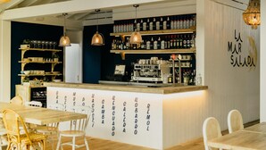 A bar area with a wooden counter, shelves of bottles, and a coffee machine. There are wicker chairs and a table in the foreground. - Stylish Chalet in Mont-roig (Mont-Roig del Camp)