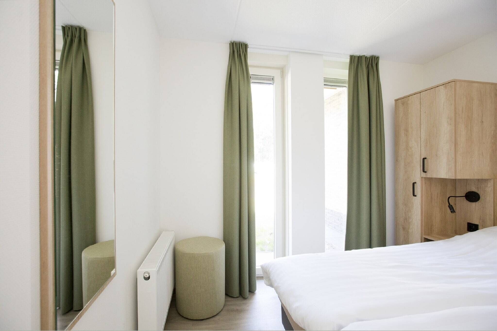 Een slaapkamer met een bed, een houten garderobe, een rond poef en een raam met gordijnen.