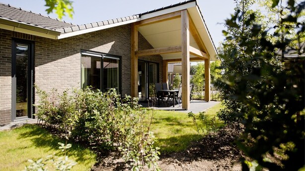 Une maison moderne dotée d’un patio couvert, d’une façade en briques et d’un jardin.