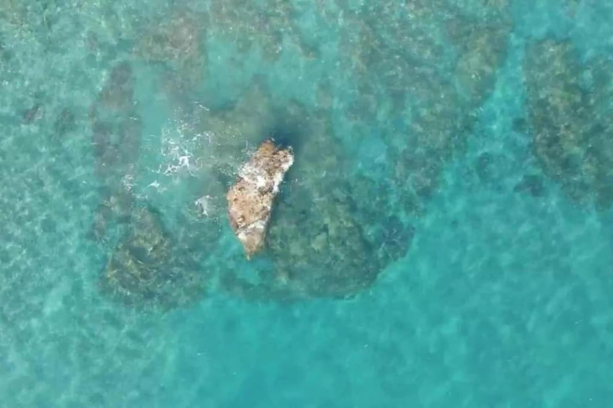 A clear aerial view of a beach with a rocky outcrop and shallow turquoise waters.