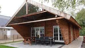 A log cabin with a covered patio area, a dining table, and chairs. - Holiday Home in Netherlands with Pond View (Baarle-Nassau)