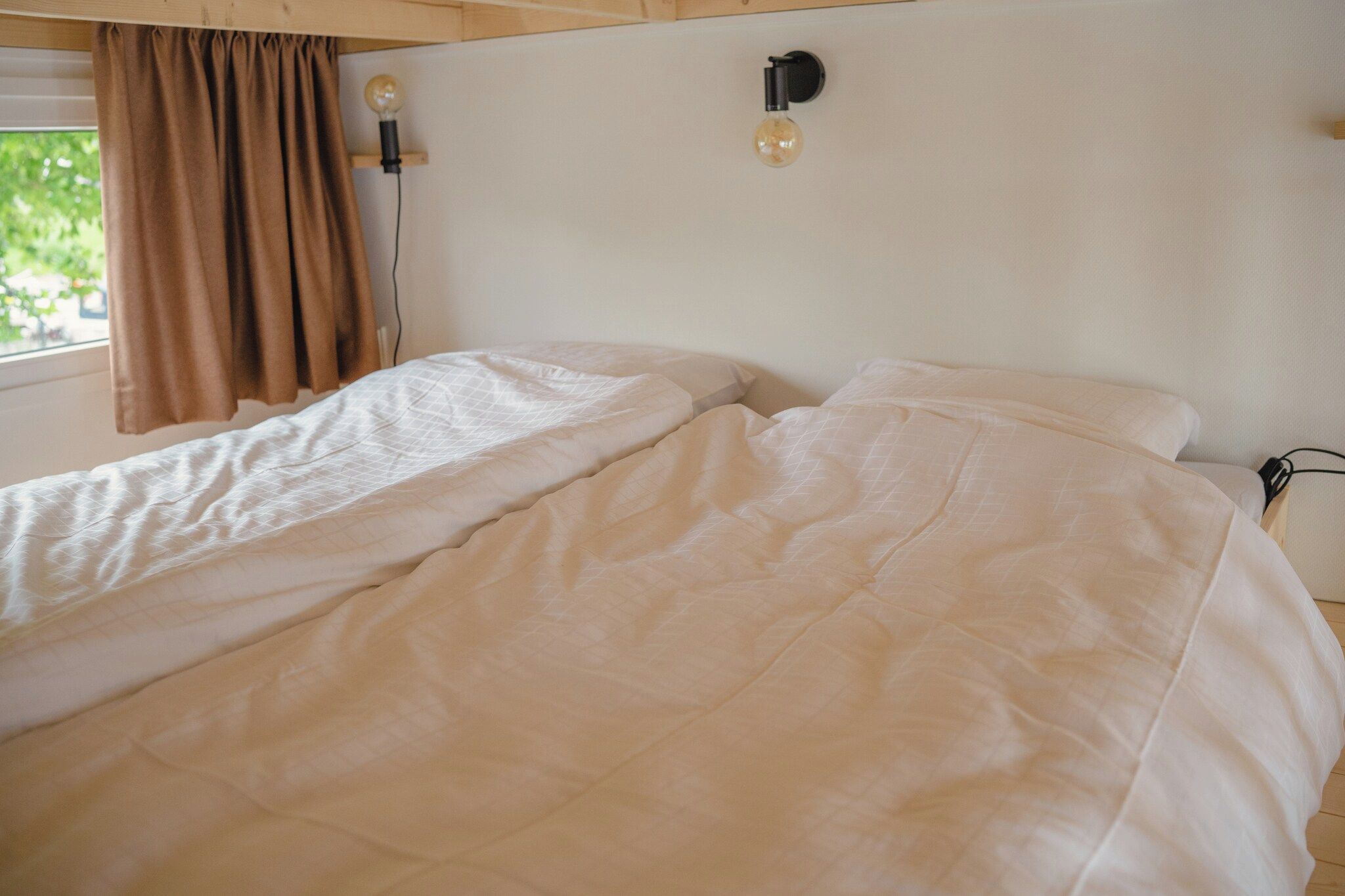 Een eenpersoonsbed met een witte dekbedovertrek in een kamer met een raam en gordijnen.