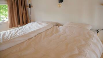 Een eenpersoonsbed met een witte dekbedovertrek in een kamer met een raam en gordijnen.