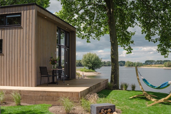 A modern wooden cabin with a deck, a hammock, and a view of a lake. - Tiny House by Dutch Waterfront Retreat (Maurik)