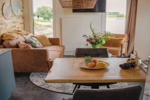 A cozy living room with a sofa, a dining table with fruit, and a vase of flowers. - Tiny House by Dutch Waterfront Retreat (Maurik)