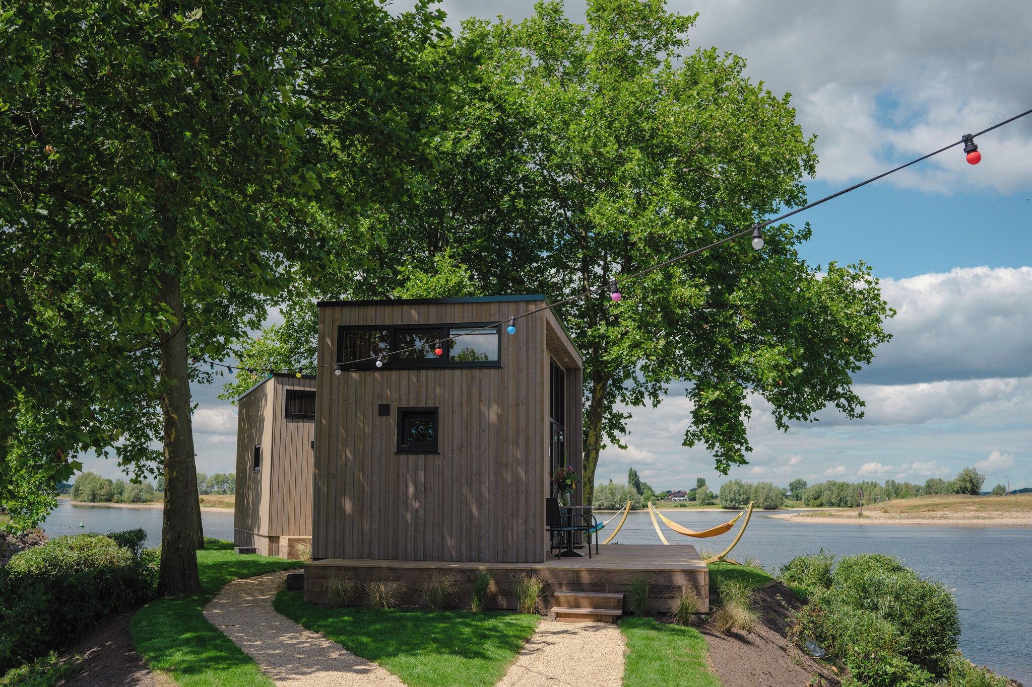 A wooden cabin with a deck, a hammock, and a view of a lake.