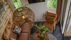 Una sala de estar acogedora con un sofá marrón, una lámpara colgante de mimbre y una pequeña mesa redonda con un jarrón de flores.