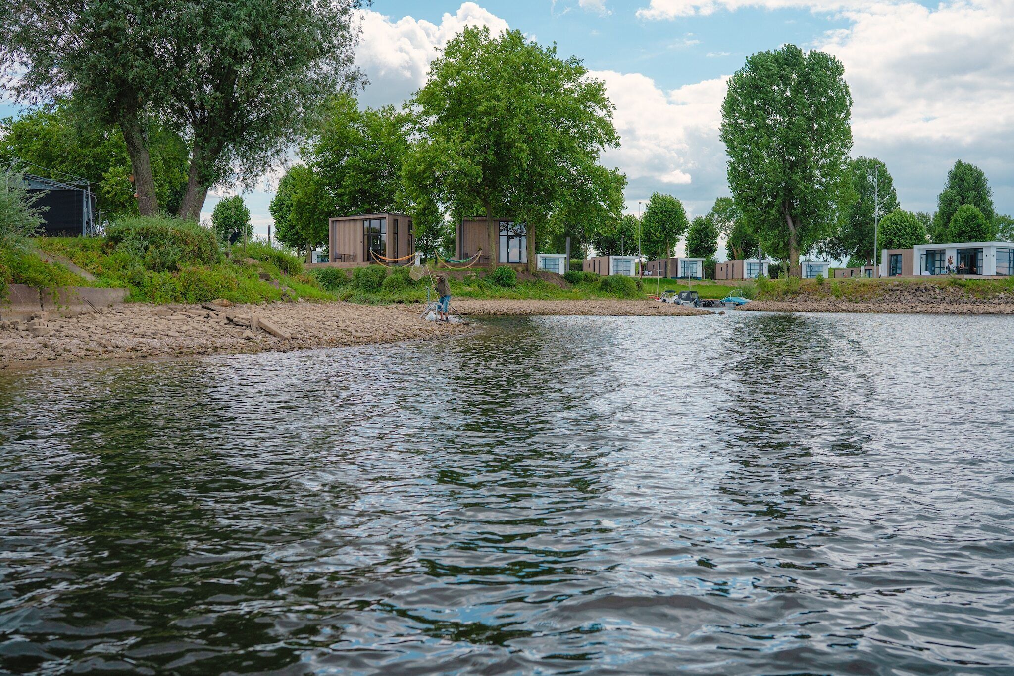 Vista sul fiume con cabine moderne e una persona che pesca.
