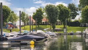 Un port esportiu amb embarcacions amarrades, un parc infantil i una zona verda amb arbres.