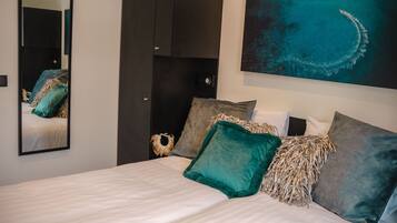 A bedroom with a bed, pillows, a mirror, a wardrobe, and a painting of a water body.