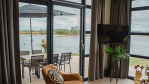 Habitació moderna amb una finestra gran, televisió i zona menjador amb taula i cadires.