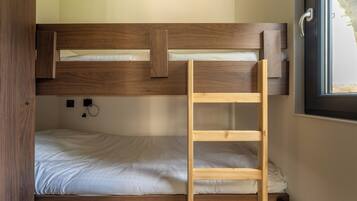 A bunk bed with a wooden ladder, a small desk with a chair, and a window with a view of greenery.
