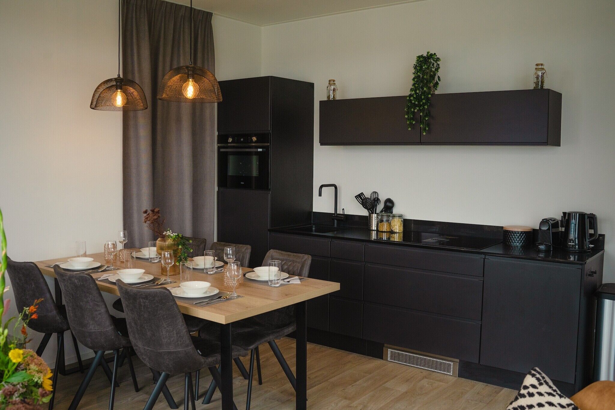 Una cocina moderna con armarios oscuros, una mesa de comedor de madera dispuesta para cuatro personas e iluminación colgante.