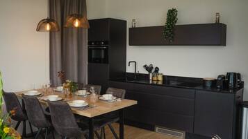 Una cocina moderna con armarios oscuros, una mesa de comedor de madera dispuesta para cuatro personas e iluminación colgante.