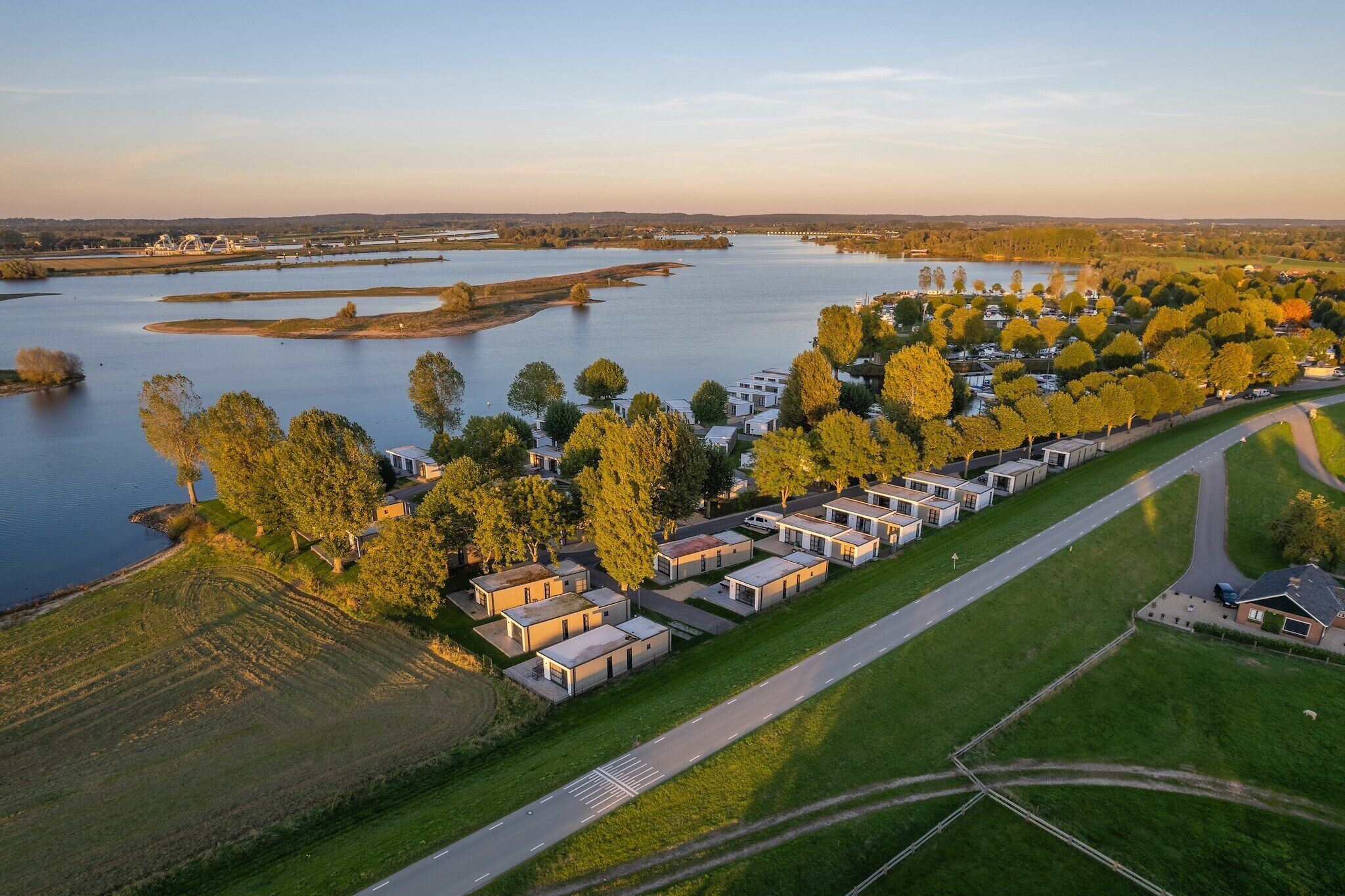 Vista aerea di un campeggio sul lago, con camper e case mobili, circondato da alberi e una strada.