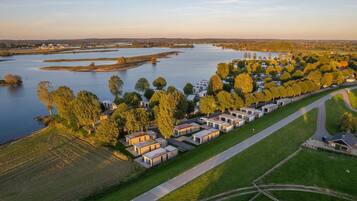Vista aerea di un campeggio sul lago, con camper e case mobili, circondato da alberi e una strada.