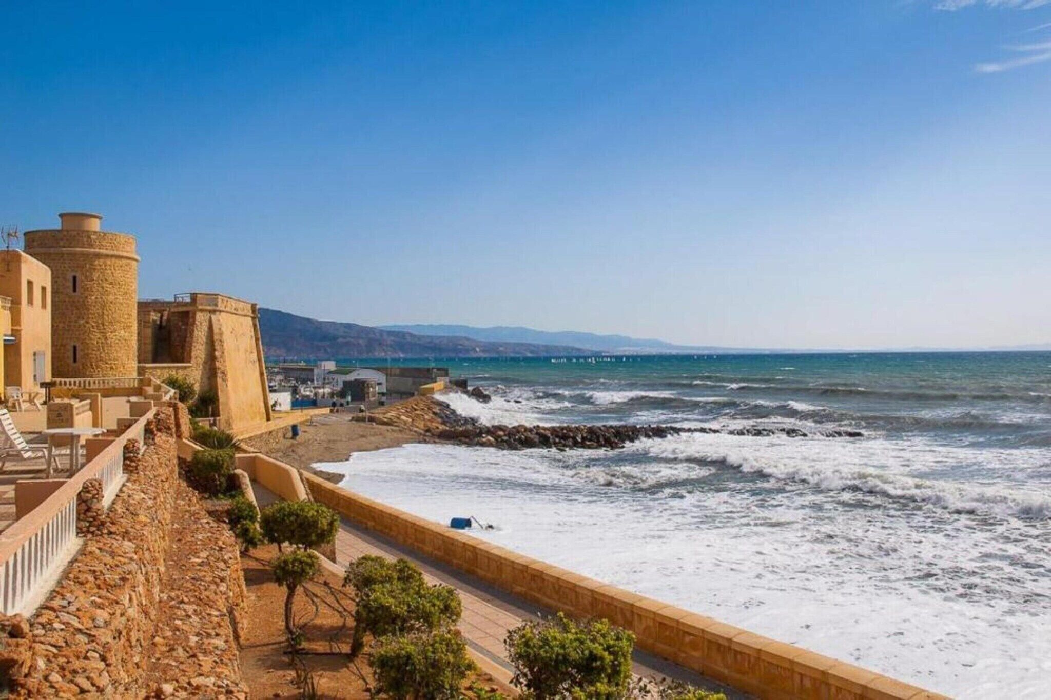 Vista costera con un edificio de piedra, una playa y el mar.
