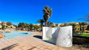 Zona de piscina con suelo de baldosas, una palmera y una estructura de pared blanca.