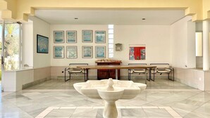 Una habitación amplia con una gran fuente de mármol, una larga mesa de comedor con sillas y cuadros de paisajes urbanos en la pared.