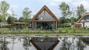 A modern house with a triangular roof, large glass windows, and a reflection in a pond.