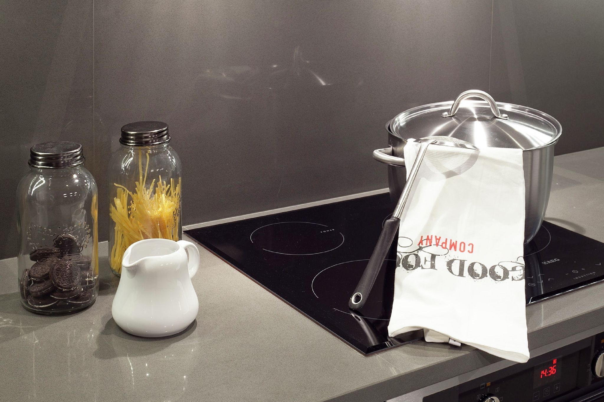 Una encimera de cocina con una estufa, una jarra blanca, dos frascos de vidrio y un saco de harina.