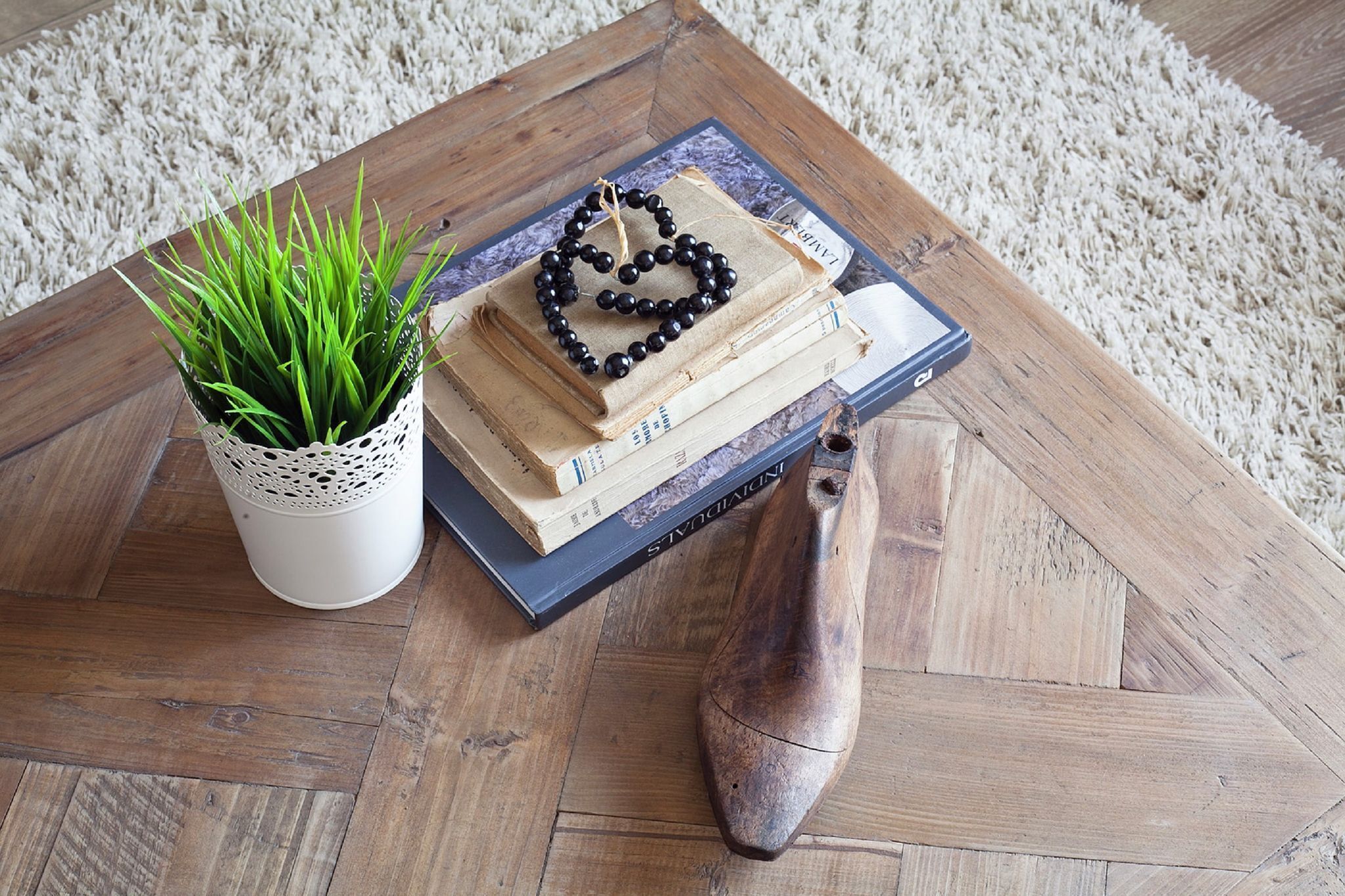 A wooden coffee table with a stack of books, a black beaded bracelet, and a potted plant.