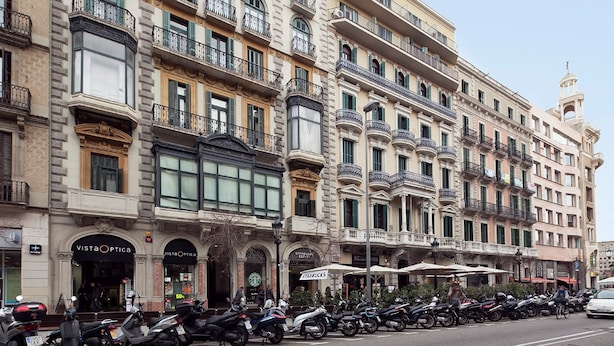 Une rangée de bâtiments historiques dotés de nombreux balcons, de boutiques, dont un Starbucks, et une rangée de motos garées.