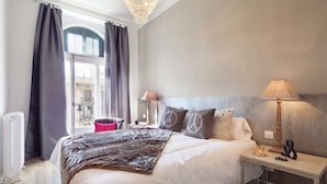 Une chambre d’hôtel avec un grand lit, deux tables de chevet, une petite table, un radiateur et une vue sur l’extérieur.