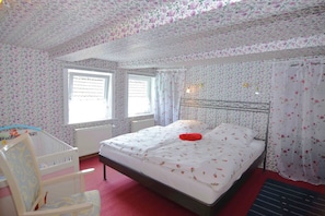 Cozy retreat with a floral-patterned bed and a comfortable chair, featuring a window with a blind and a radiator.