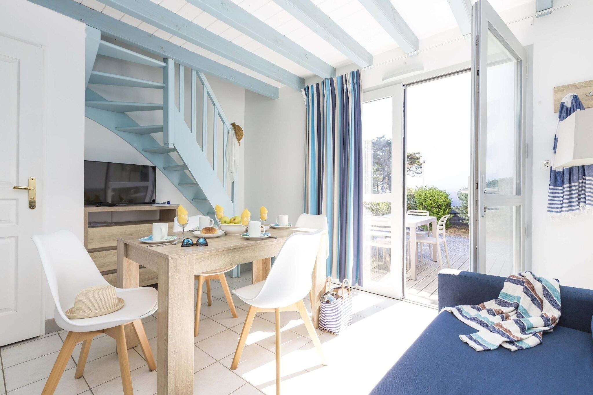 Une cuisine moderne avec un coin repas, un escalier et une vue sur l’extérieur, accessible par une porte vitrée.