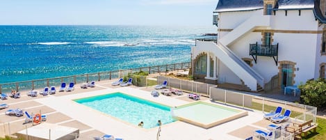 A pool area with multiple sun loungers and a clear view of the ocean.