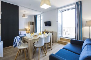 A modern hotel room with a dining area, a sofa, and a TV mounted on the wall.