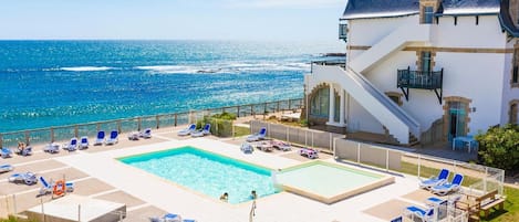 A hotel with a pool area, lounge chairs, and a view of the ocean.