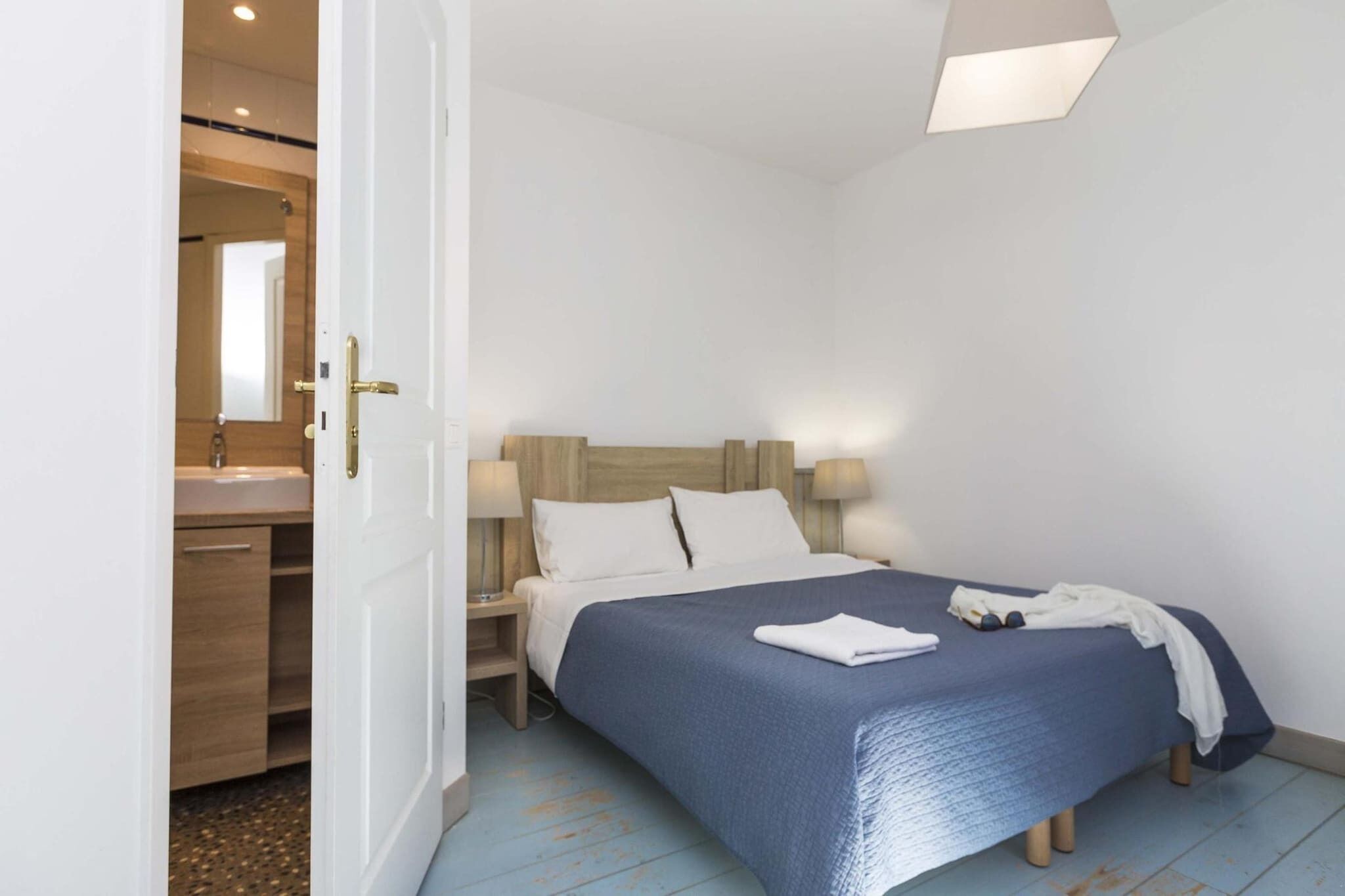 A bedroom with a bed, bedside lamps, a nightstand, and a wooden headboard.