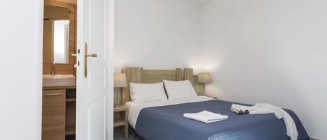 A bedroom with a bed, bedside lamps, a nightstand, and a wooden headboard.