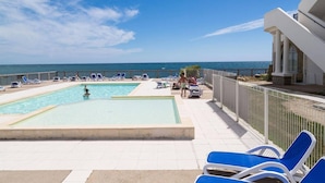 Zona de piscina con dos piscinas, sillas de descanso y vistas al mar.