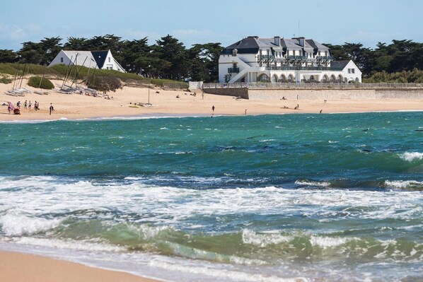 A beach with a large white building with multiple balconies and a sandy shore.