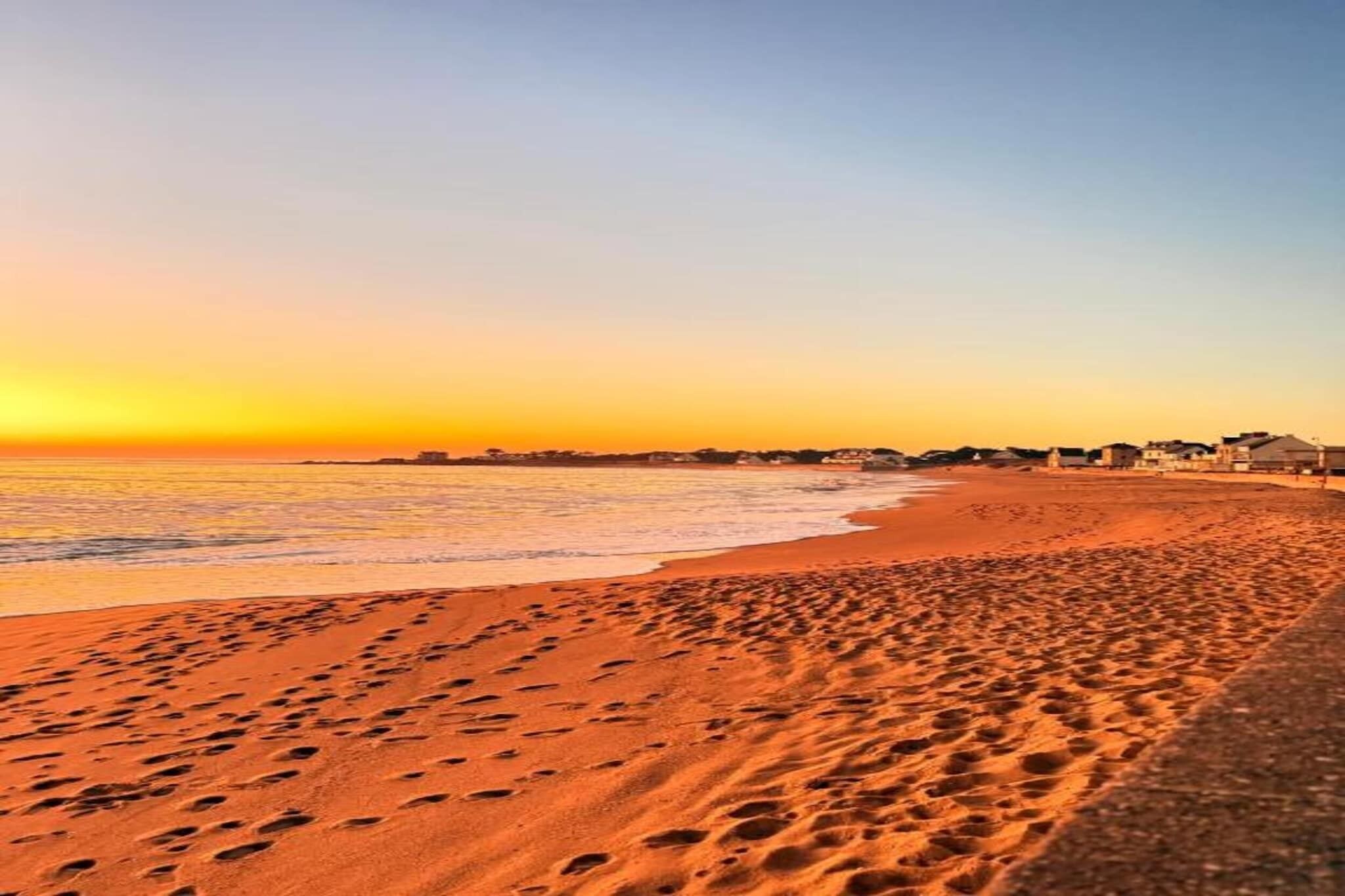Una spiaggia con impronte che conducono all'acqua, un cielo sereno e edifici in lontananza.