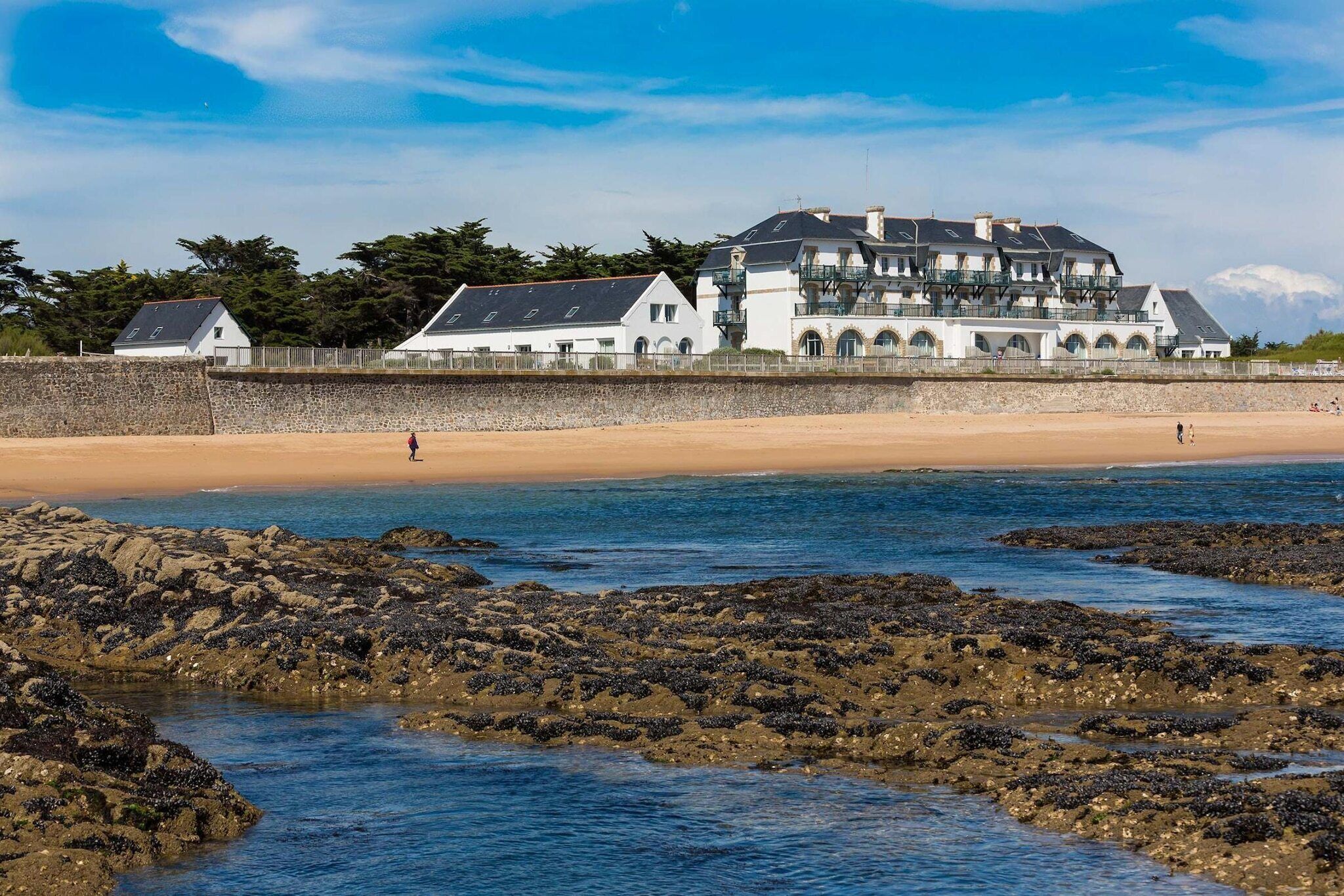 A coastal building with multiple balconies, a sandy beach, and rocky shoreline.