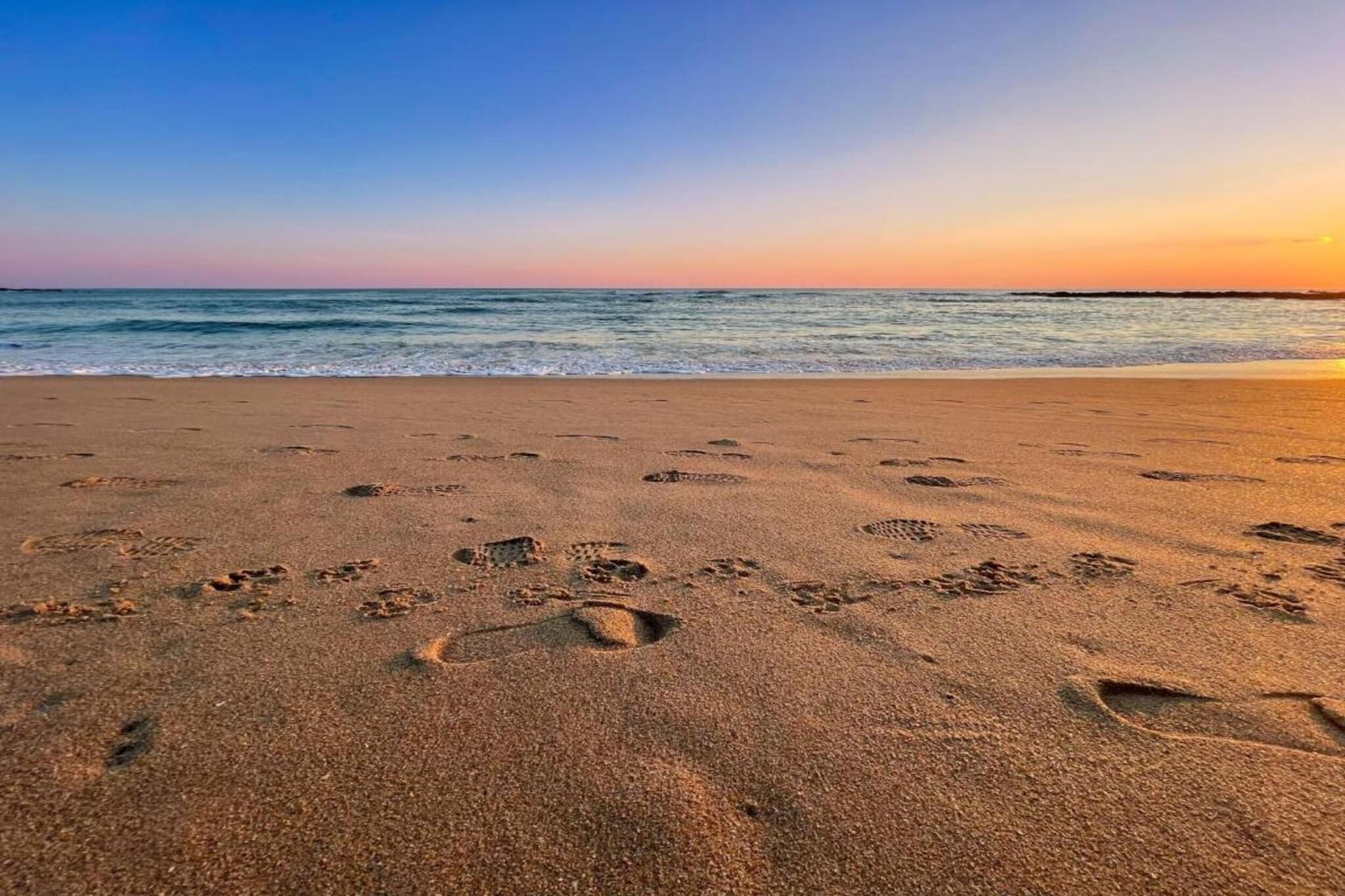 A beach with footprints in the sand and the ocean in the background.