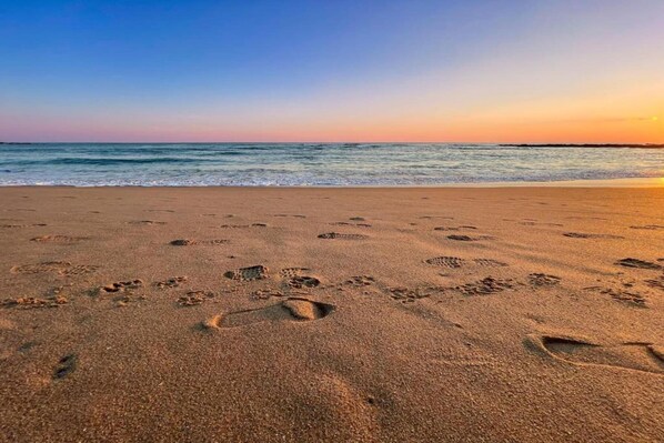 Une plage où l’on voit des empreintes de pas dans le sable, avec l’océan en arrière-plan.
