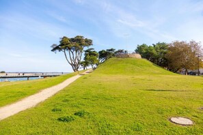 Un parc verdoyant avec un sentier menant à une colline, des arbres et une étendue d’eau en arrière-plan.
