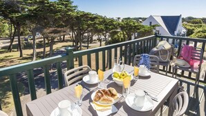 Taula preparada per esmorzar amb croissants, fruita i begudes a un balcó amb vistes a un jardí.