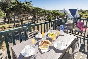 Tavola imbandita per la colazione con croissant, frutta e bevande su un balcone con vista su un giardino.