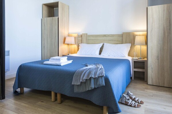 A hotel room with a bed, two bedside tables, a lamp, a pair of shoes, and a folded towel.