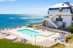 A hotel with a pool area, lounge chairs, and a view of the ocean.